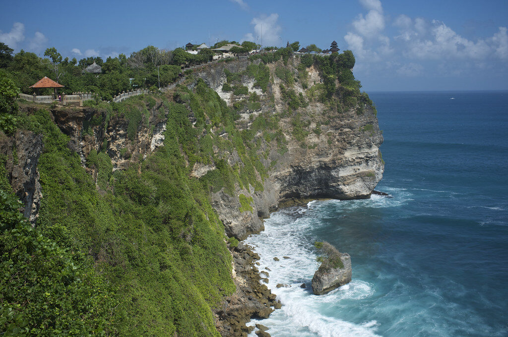 A clifftop temple pavilion perched on the peninsula's edge, the cliffs curving away below.