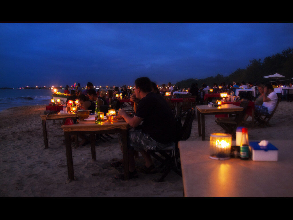 Seafood tables set out on the sand at dusk, lit by lanterns — the Jimbaran evening you come for.