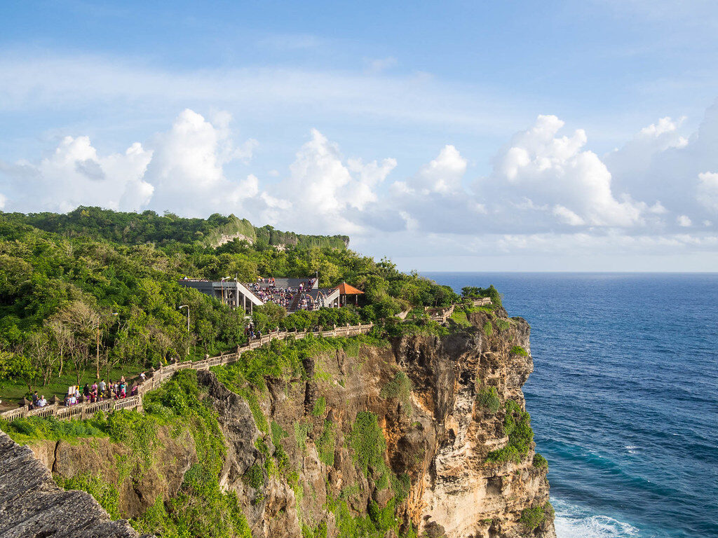 The clifftop path visitors walk between the temple gates, sea on every side.