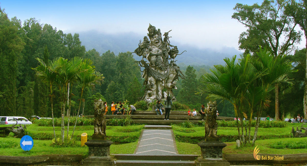 A statue and clipped gardens inside the Kebun Raya, palms rising behind.