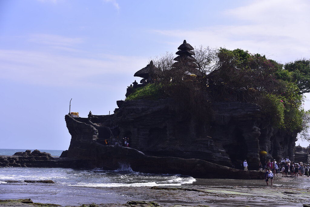 The temple on its rock as the waves break around it and the crowds gather along the shore.
