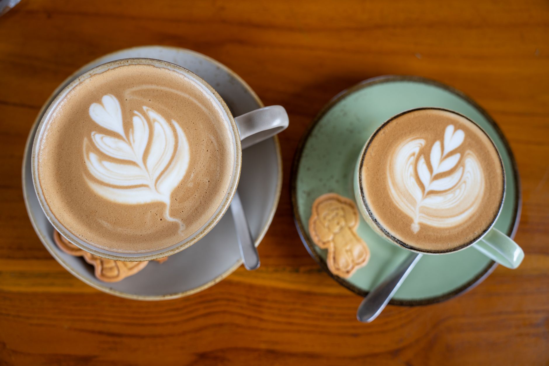 Two cups of latte-art coffee with cookies on wood