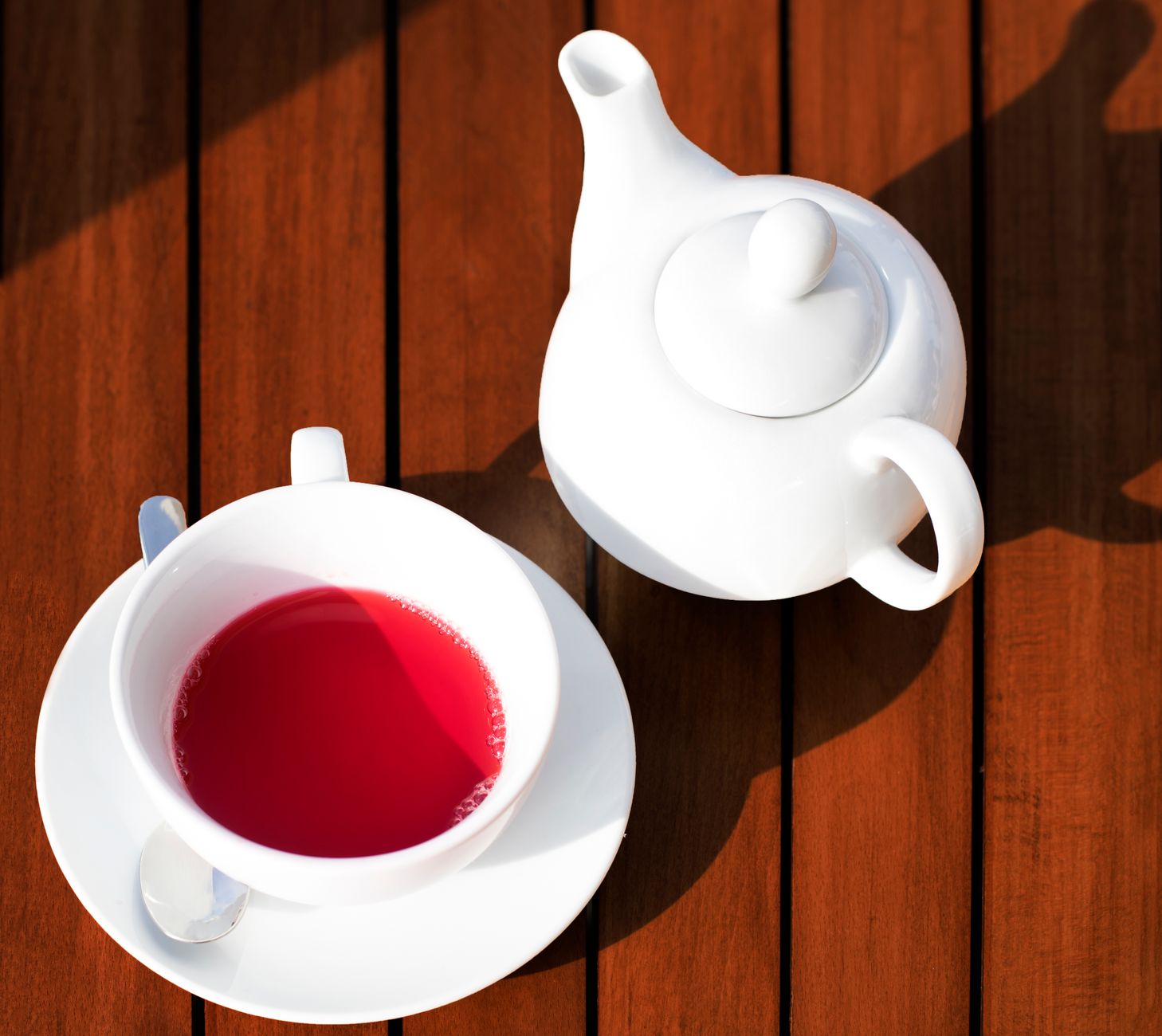 A white teapot and cup of deep-red hibiscus (rosella) tea