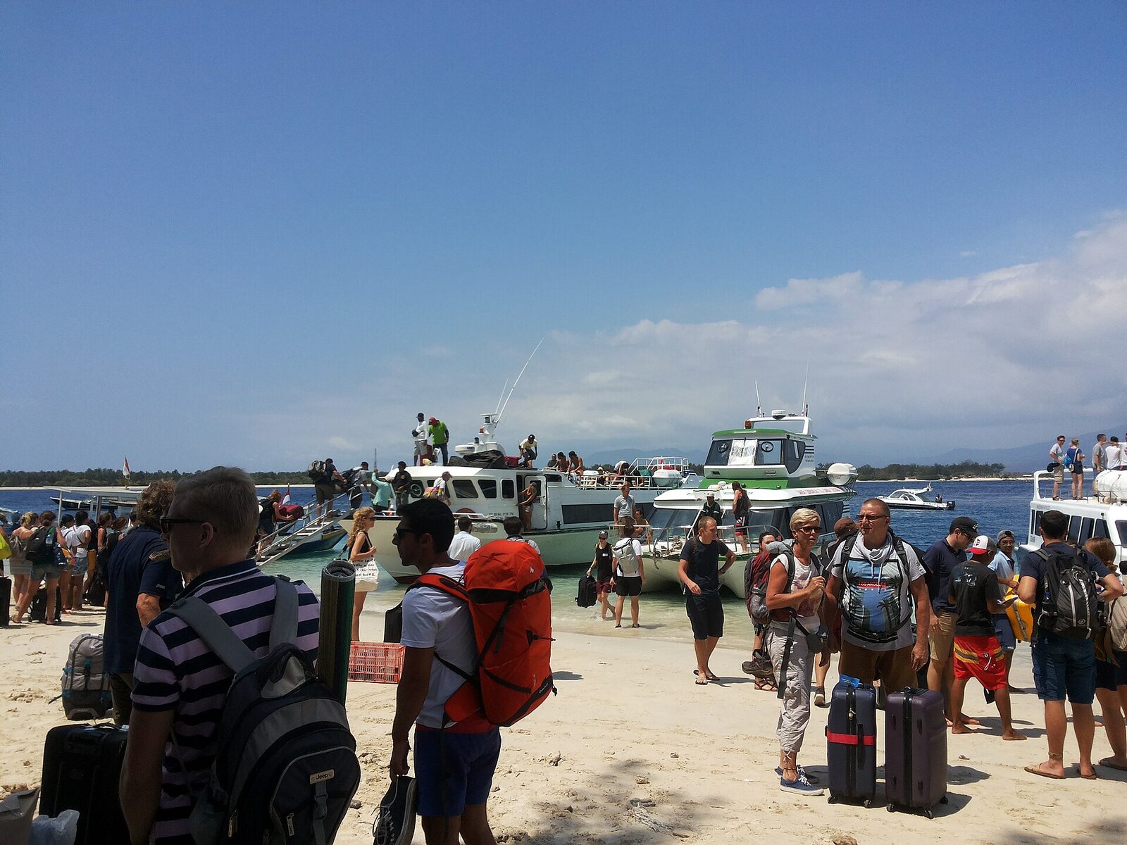 Travellers with their bags wading out to board a fast boat off the beach — the crossing to Nusa Penida, Lembongan or the Gilis.