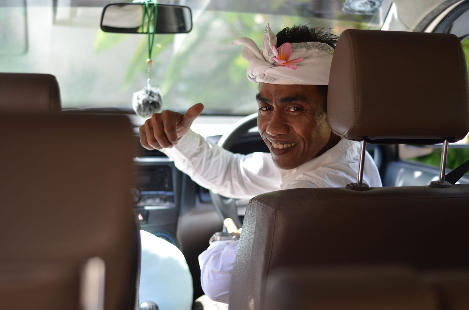 The friendly driver at the wheel, thumbs up from the front seat — the classic Bali day: one local, one car, wherever your plan goes.