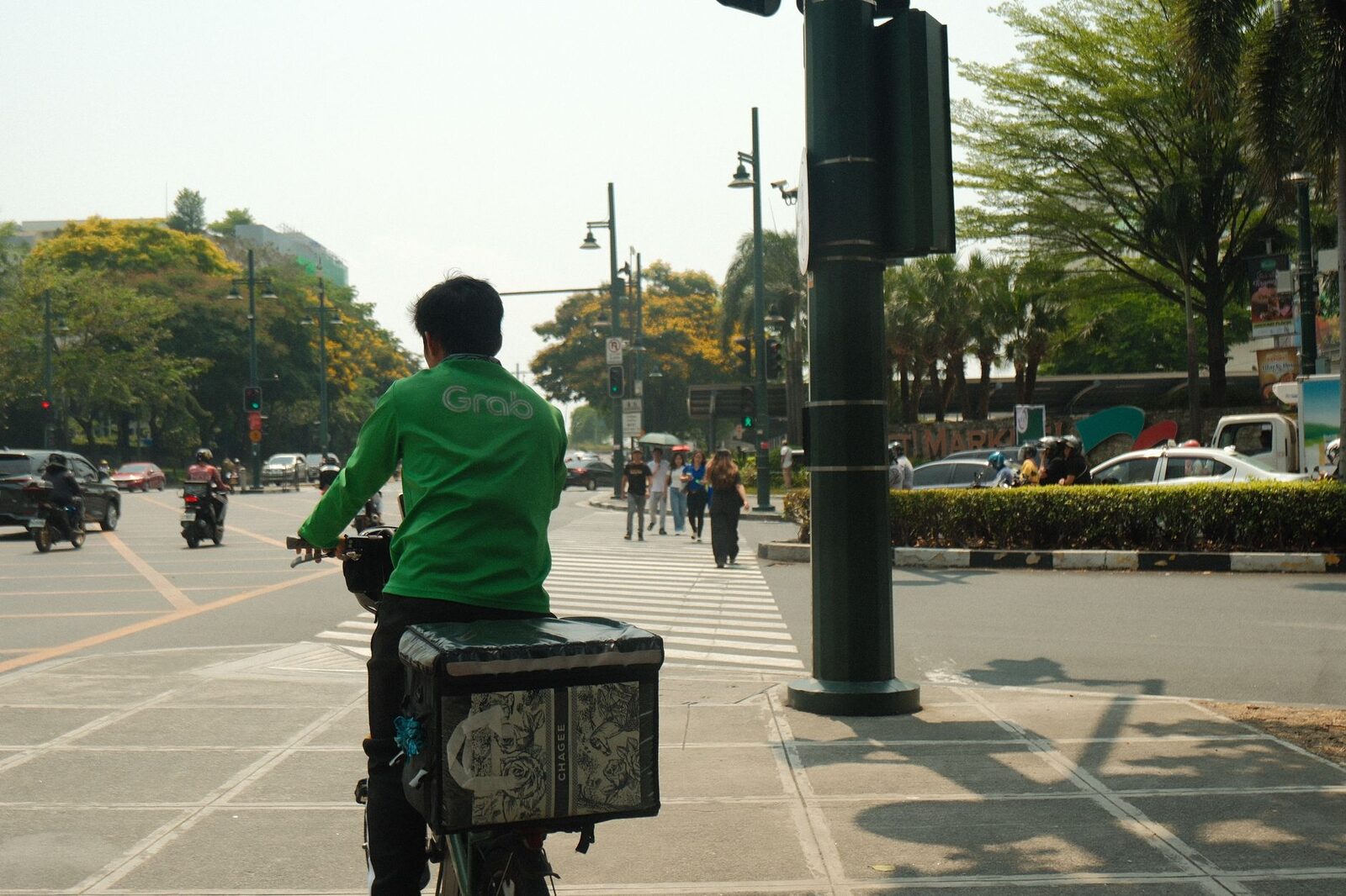 A green-jacketed rider with a delivery box heading off through the street.