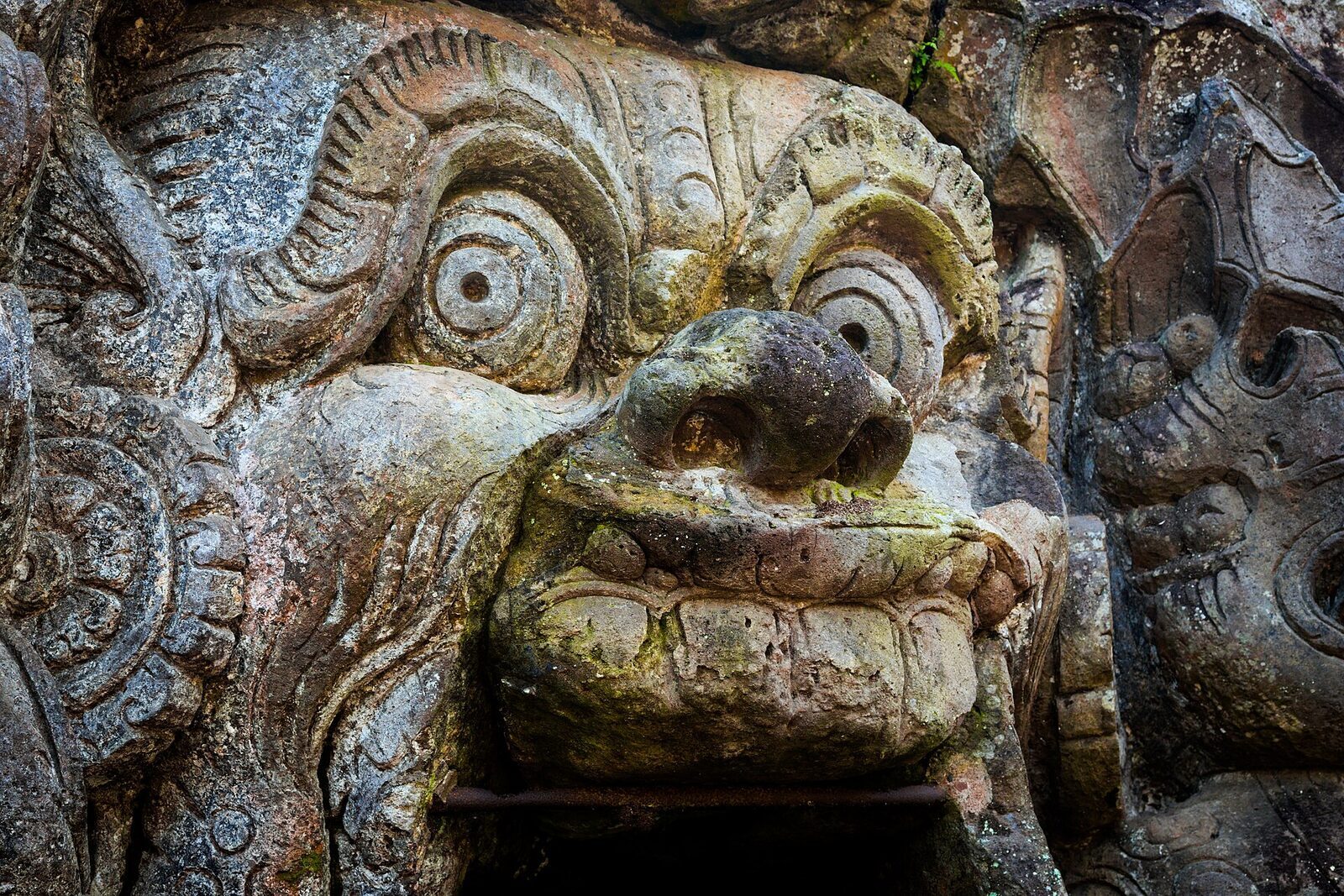 The face up close: bulging eyes and clawed hands framing the low entrance.