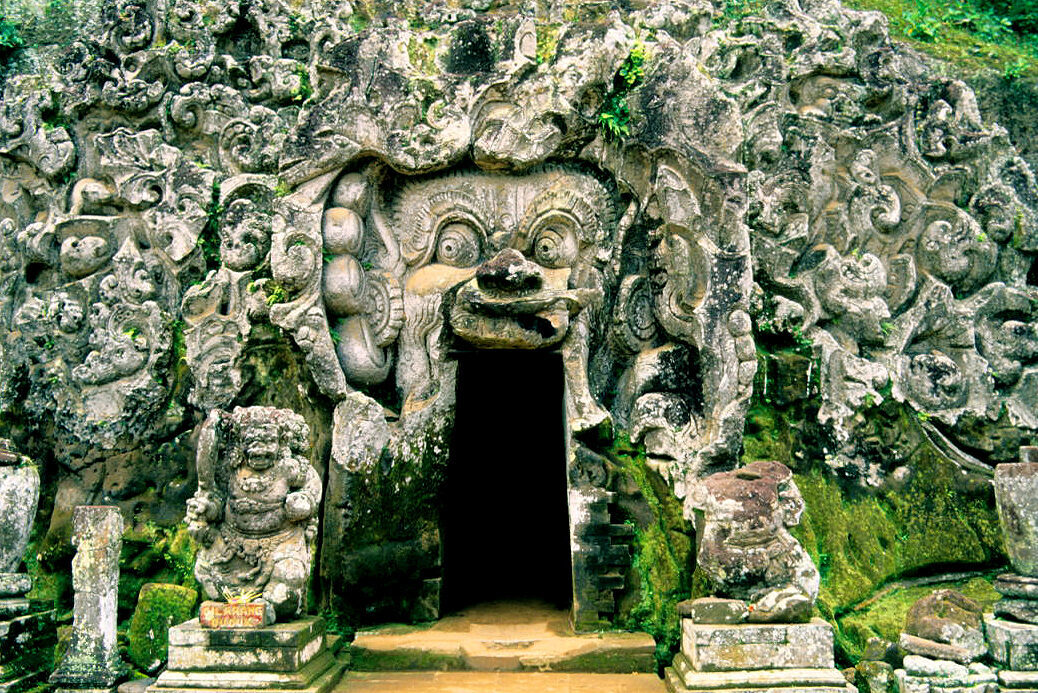 The carved cave mouth at Goa Gajah — swirling stone shaped into a gaping, demon-like face, its lips forming the doorway you actually duck through.