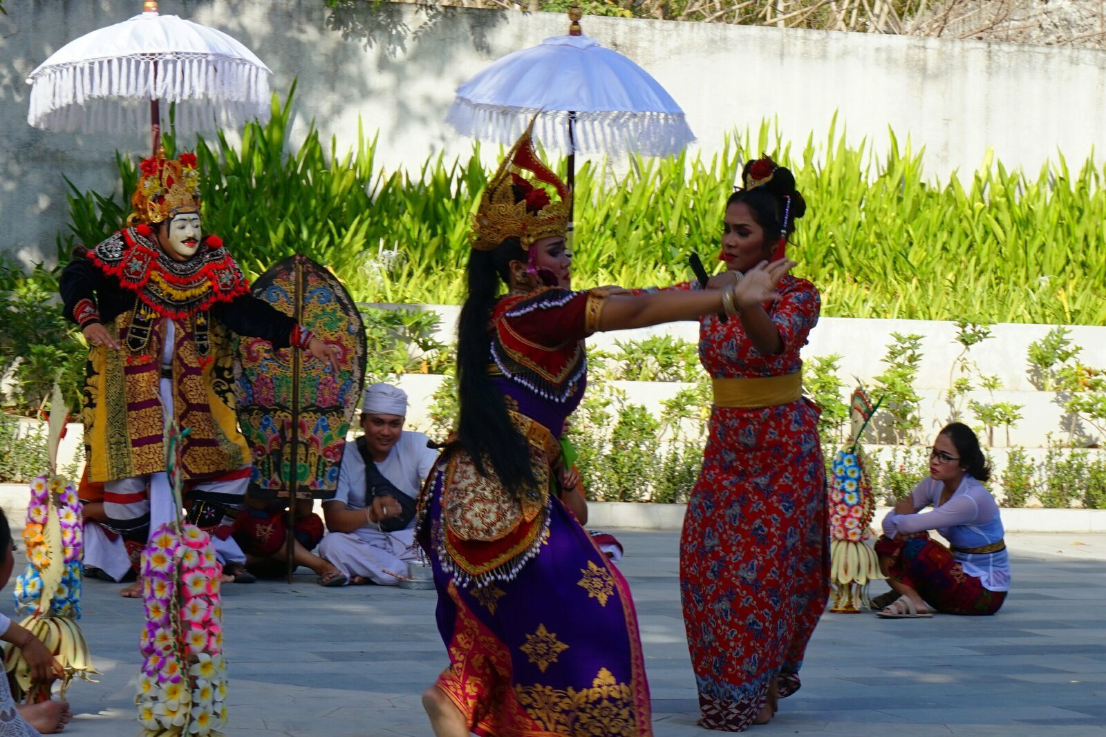 Masked and costumed dancers with ceremonial parasols — a daytime welcome dance.