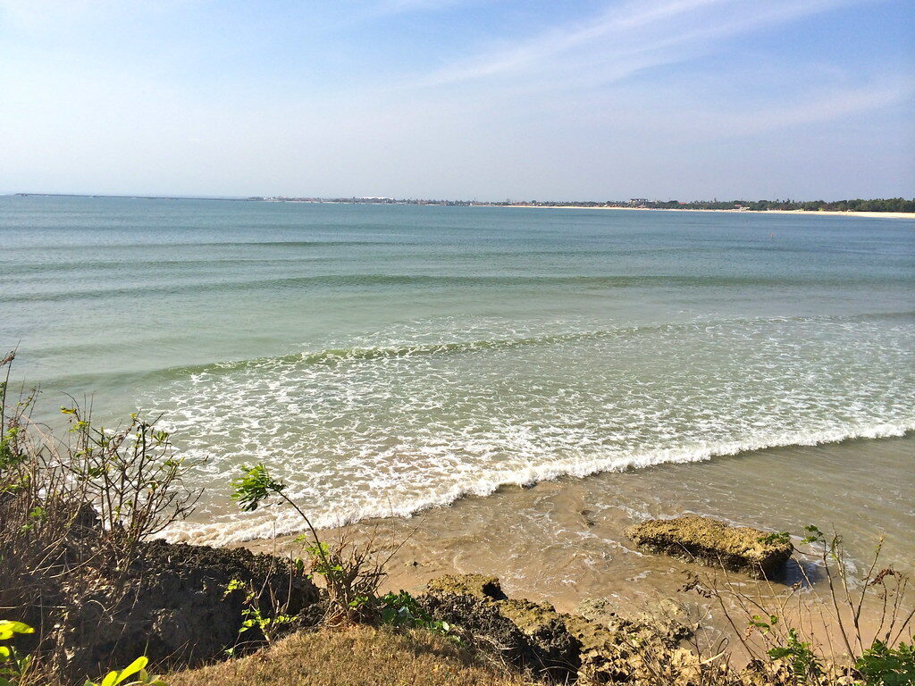 A panorama of the crescent bay, the water flat and the headland in the distance.
