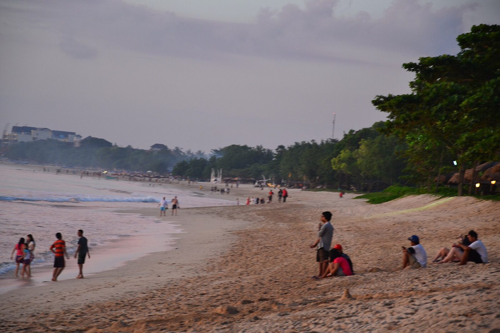 The broad grey-gold beach with people out on the sand.