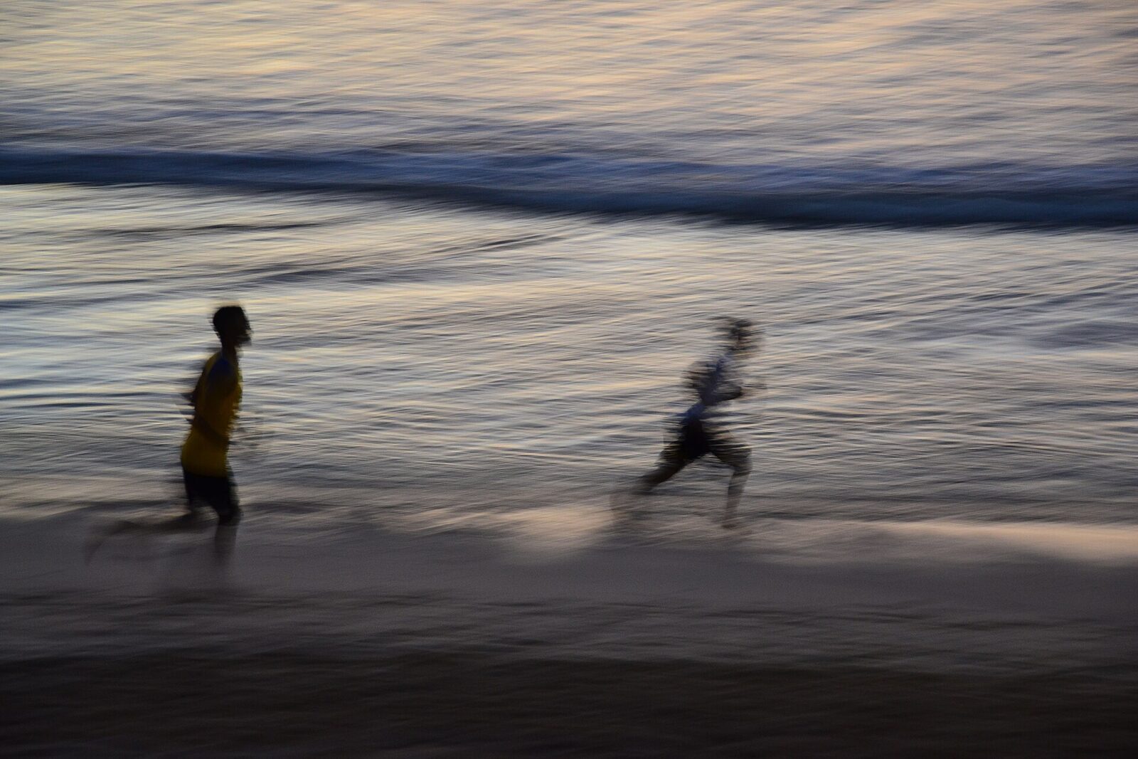 Two figures running along the wet sand at dusk.