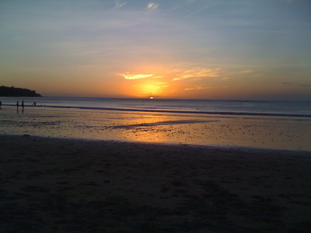 The sun low over the wide beach, its light mirrored on the wet sand.