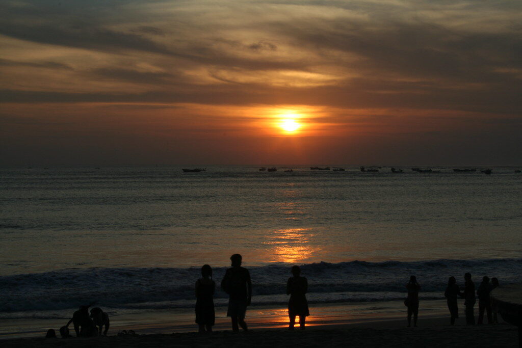 People silhouetted on the sand as the sun drops over the bay.