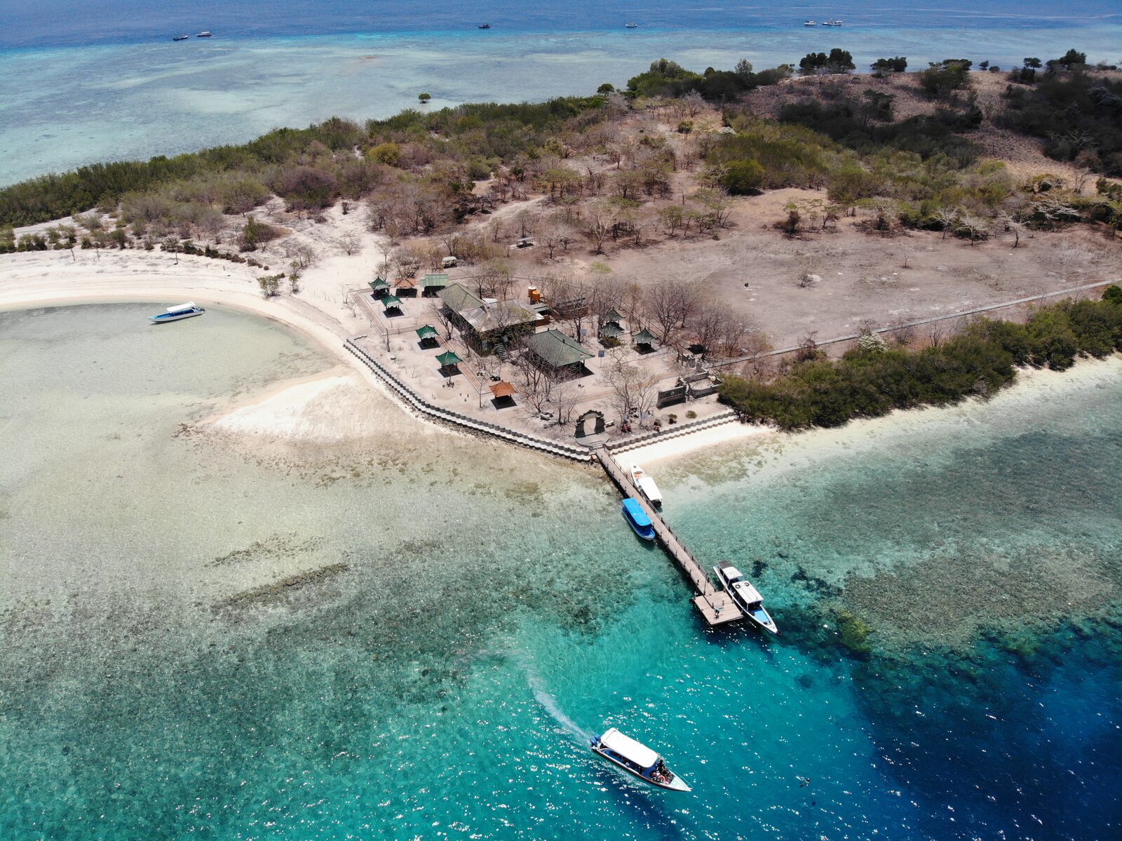 Aerial over the islet's sandy spit and jetty, ringed by turquoise reef in West Bali National Park.