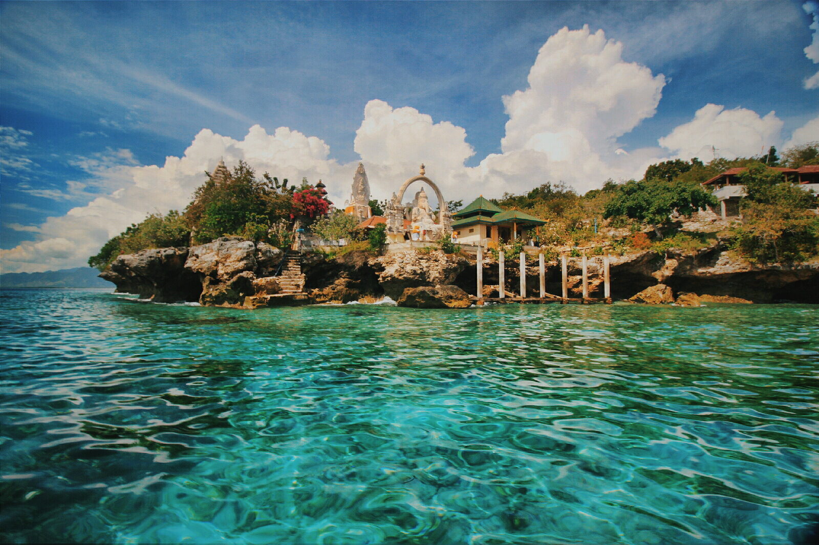 A tiny shrine perched on a coral outcrop off the island, the reef glowing turquoise around it.