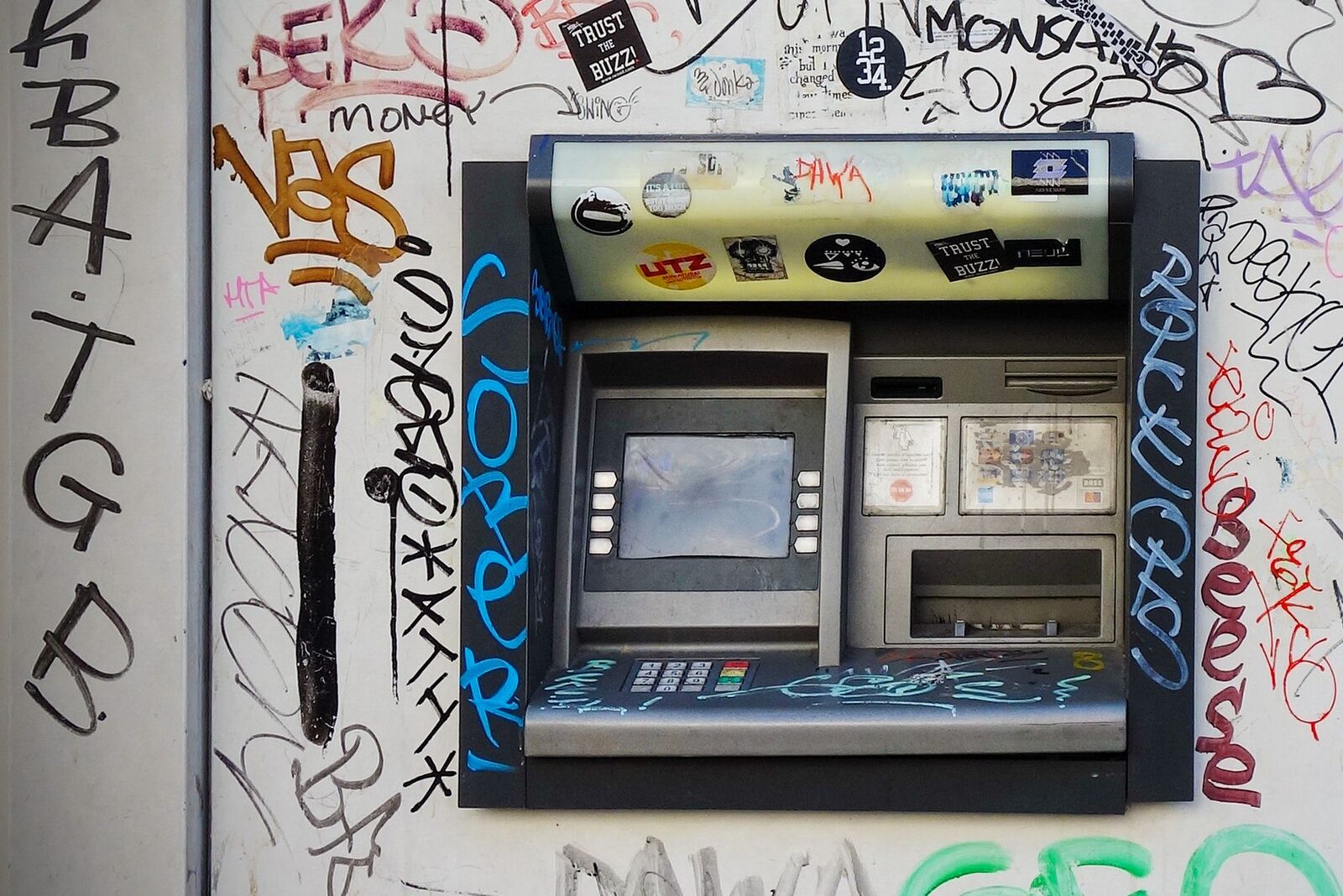 A sticker-covered street ATM. Give the card slot a wobble before you insert; skimmers are stuck on and often wiggle loose.