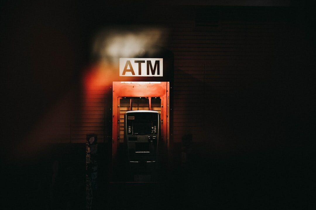 A lone ATM glowing on a dark street — exactly the machine to walk past. Skimmers get clipped onto quiet boxes like this one.