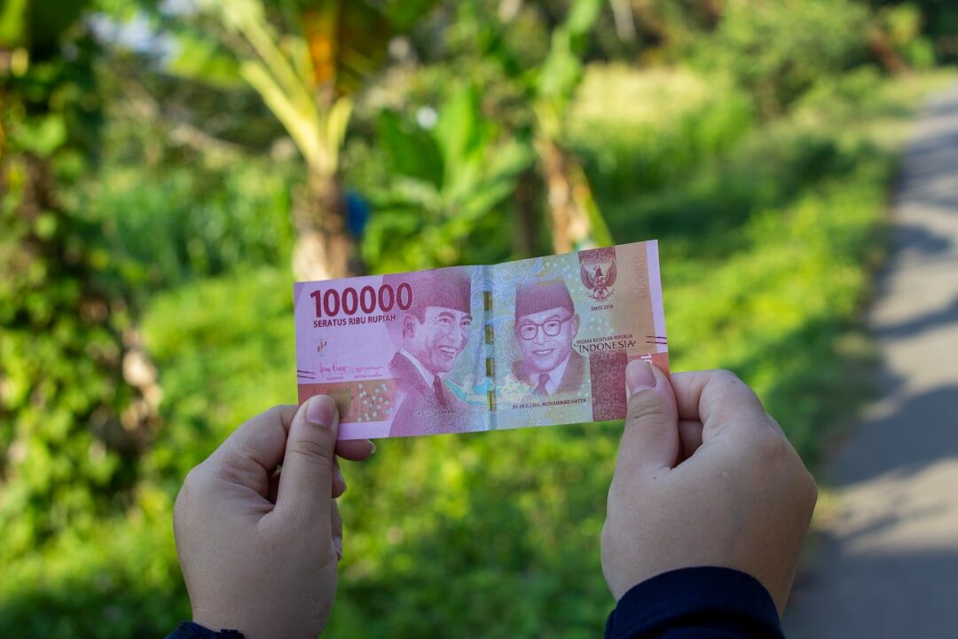 Holding a single red 100,000 note — the moment you technically become a millionaire, and the note worth slowing down to count.