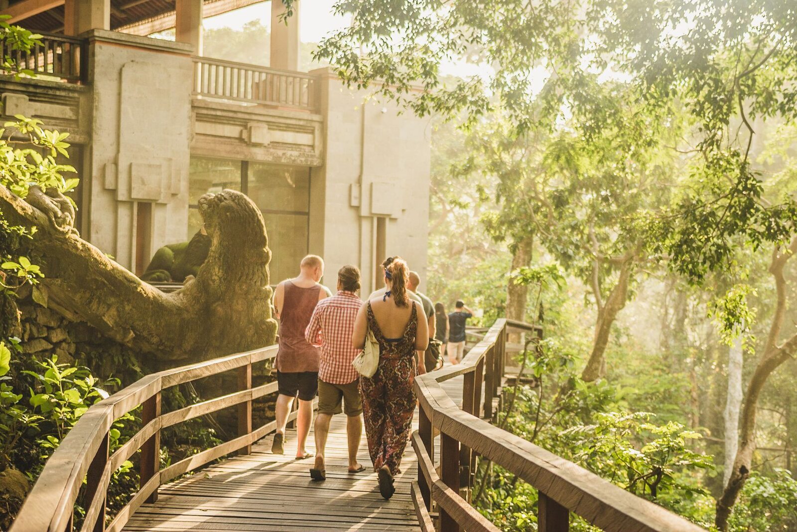 A wooden footbridge in dappled light, visitors crossing through the trees.