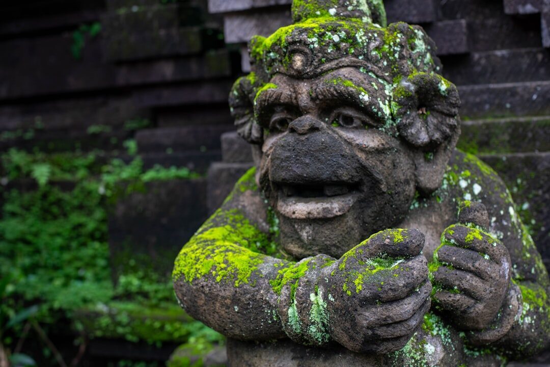 A guardian statue furred with bright green moss, grinning out from the temple stone.