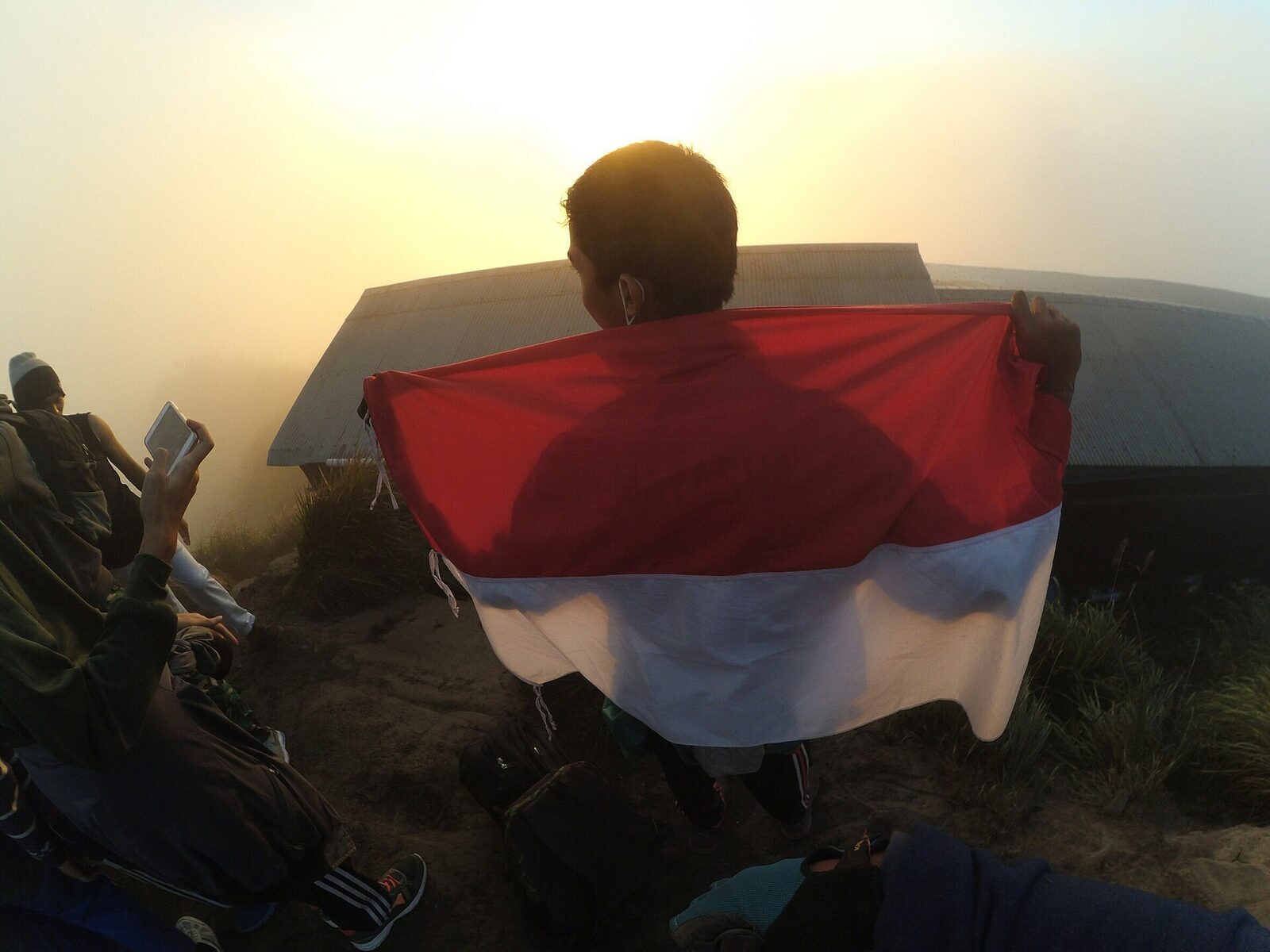 A climber with the Indonesian flag on Batur's summit at dawn.
