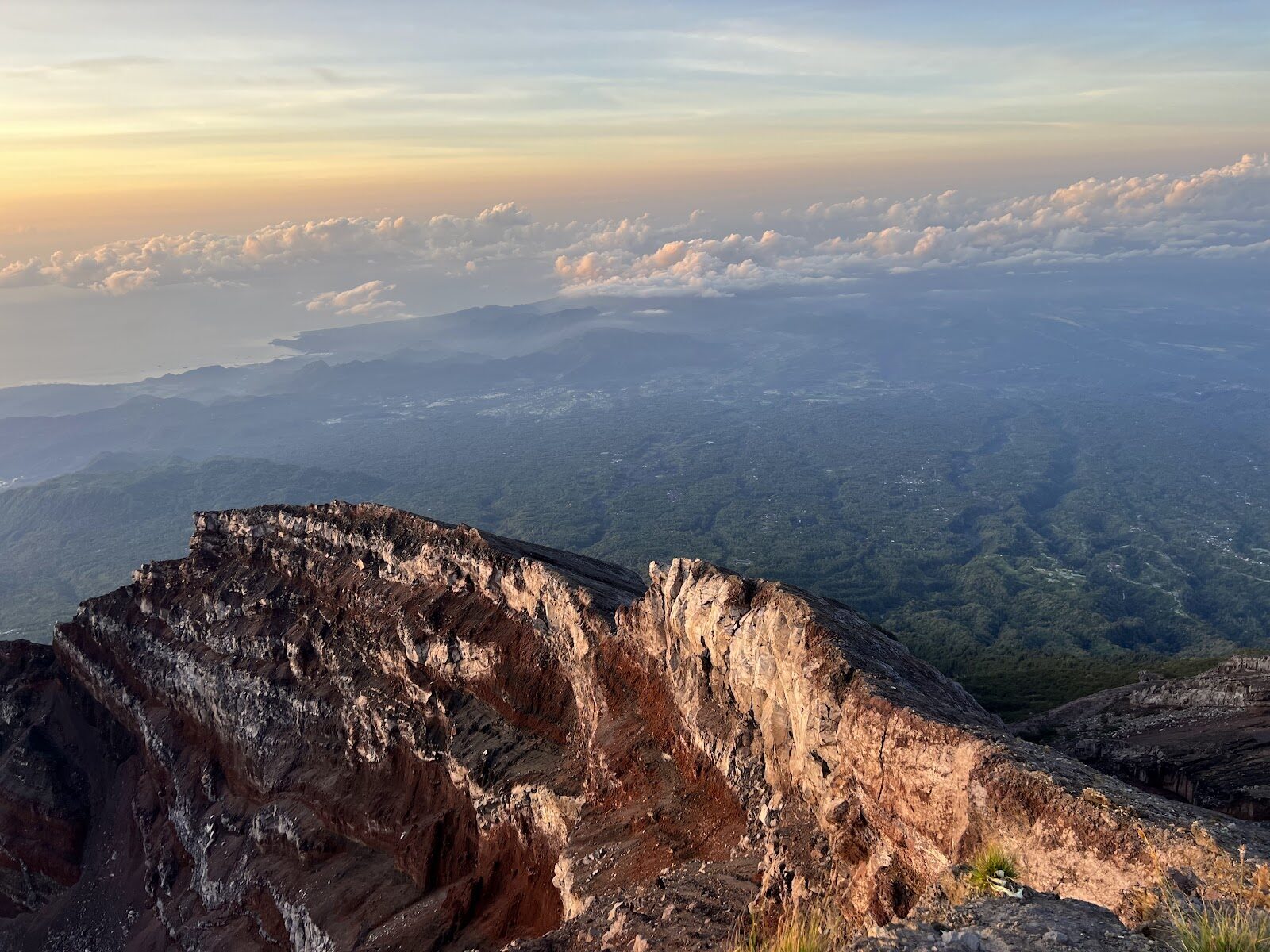 The top of Agung at first light — bare rock falling away to a sea of cloud, the island floating below. This is what the midnight climb is for.