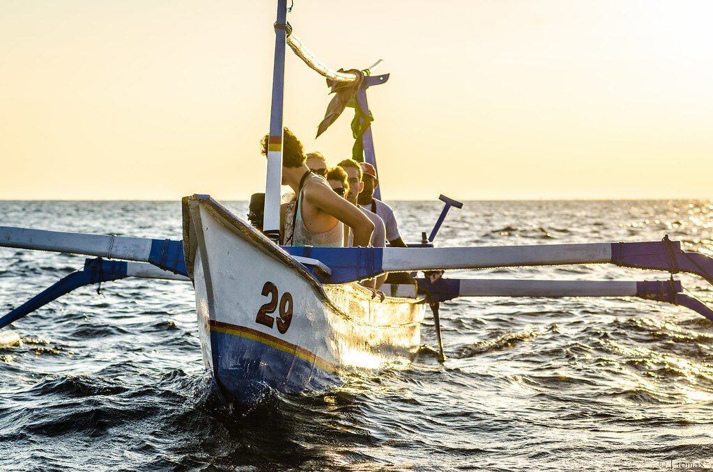 A dolphin-tour outrigger heading out at sunrise, loaded with hopeful watchers — the small jukung boats that run the dawn runs.