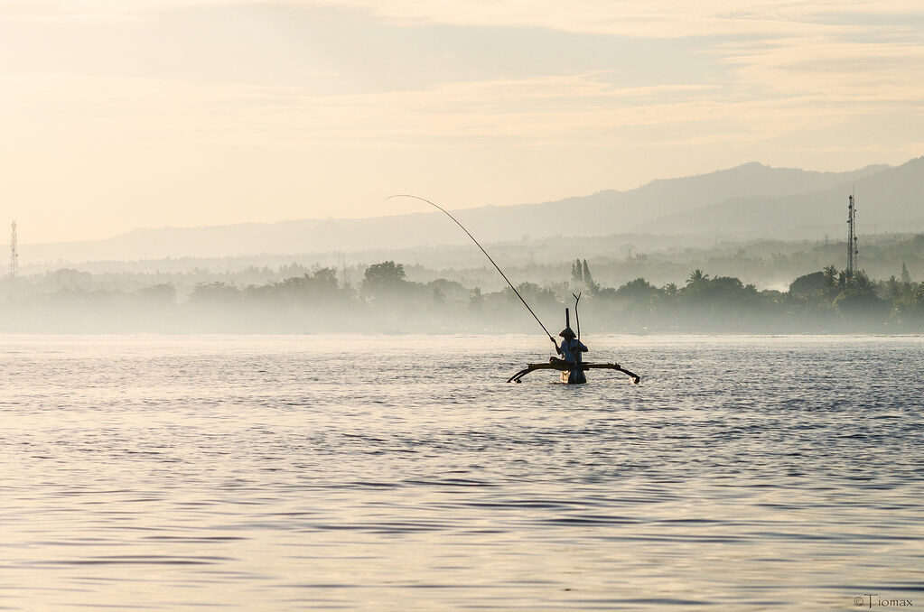 A lone fisherman on the glassy dawn sea off Lovina — the slow, un-fussy pleasure that outlasts the dolphins.