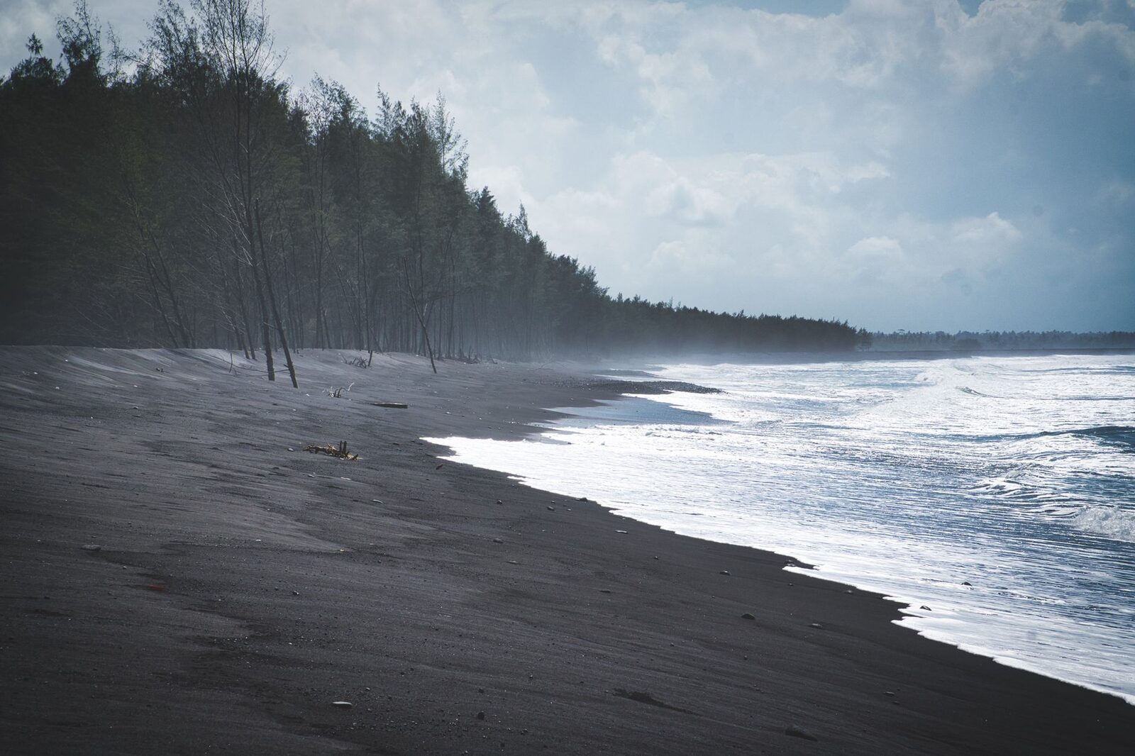 Grey-black volcanic sand and open water on the north coast — the colour that catches first-timers off guard.