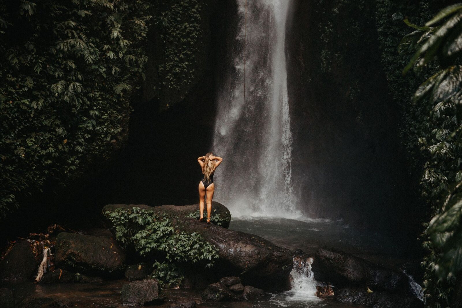 A figure dwarfed at the foot of a tall fall — the scale these gorge waterfalls run to. (A north-Bali waterfall.)