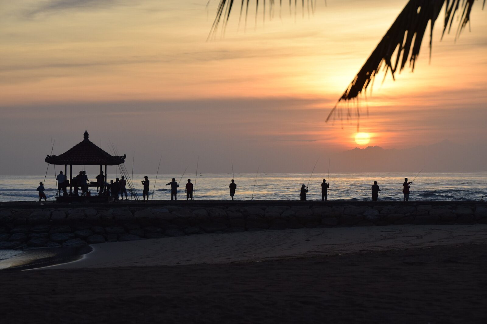 The Nusa Dua gazebo at sunrise, a row of early walkers on the sand.