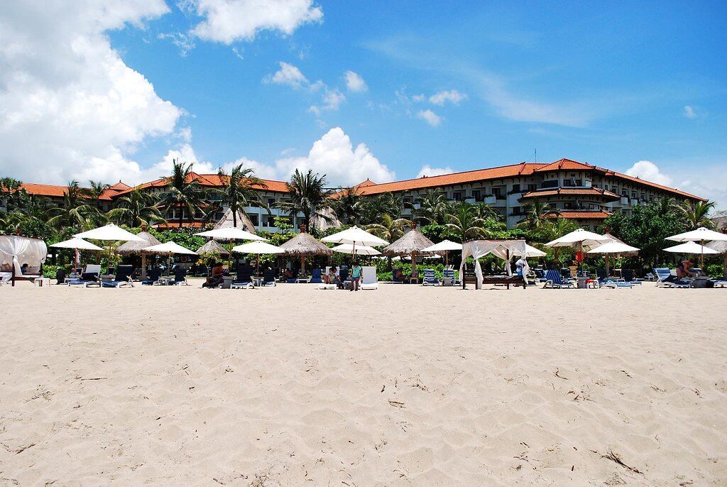 Loungers set out on a resort beachfront, red-roofed hotels behind.