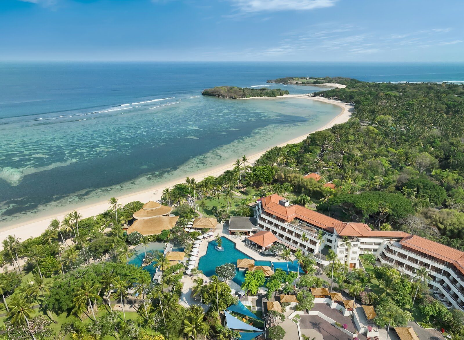 Nusa Dua from the air — resort roofs, pools and manicured grounds fanning out behind the beach. This is the planned enclave, by design.