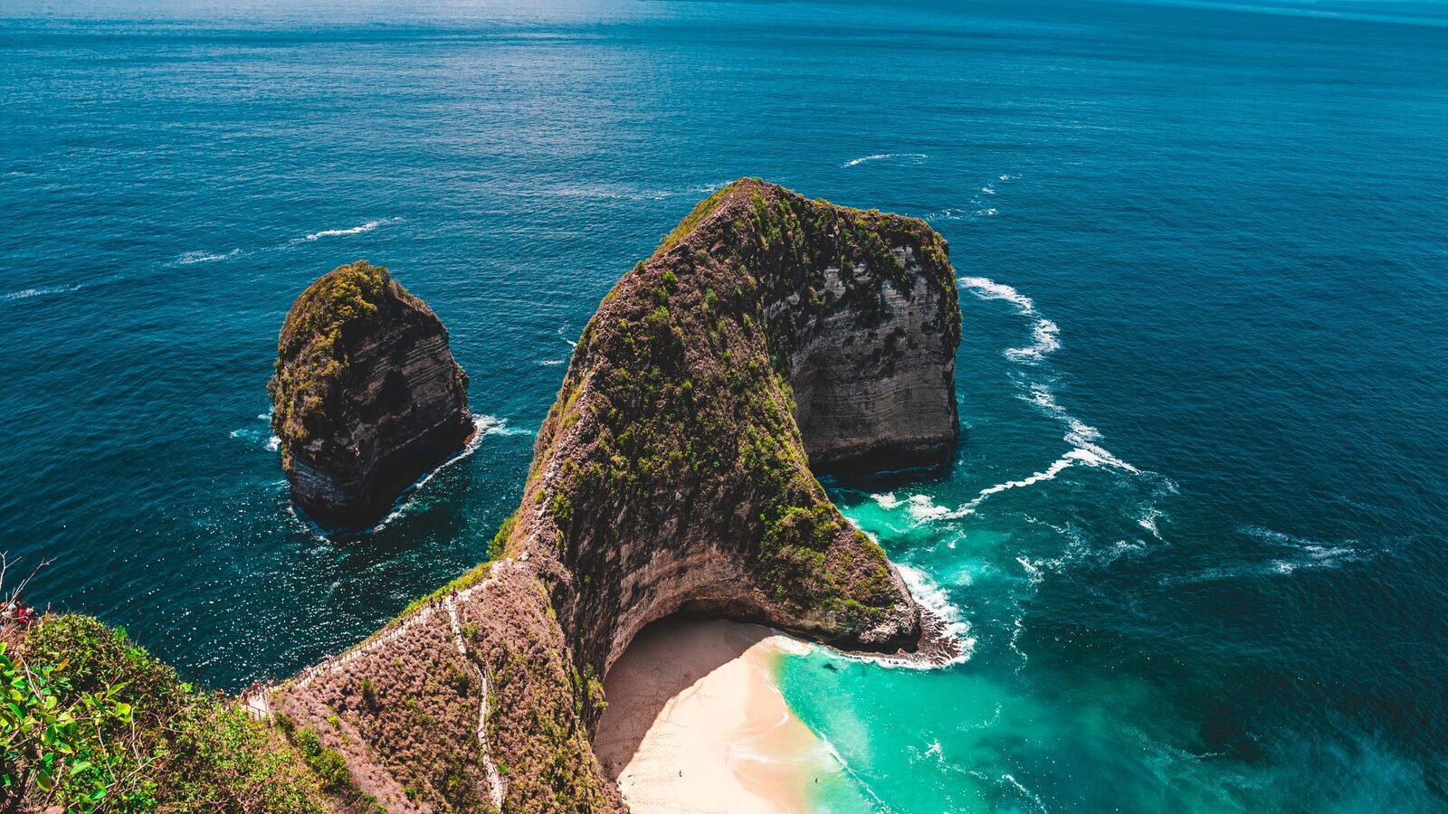Kelingking from above, the turquoise cove wrapping the foot of the cliff.