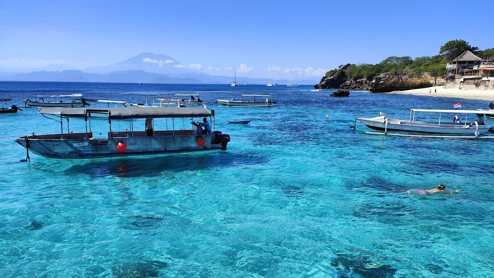 Outriggers on the water, a mountain rising across the strait toward mainland Bali.