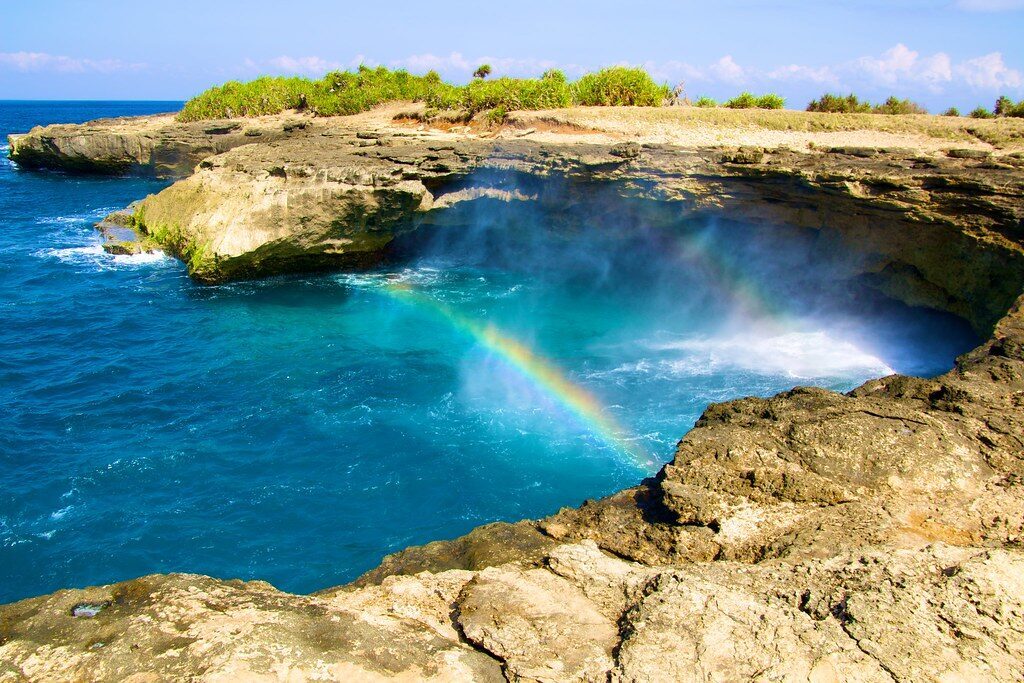 A rainbow hanging in the spray as the sea forces up through the rocks at Devil's Tear.