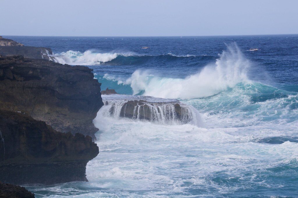 A wave breaking clean over the flat rock shelf below the cliff.
