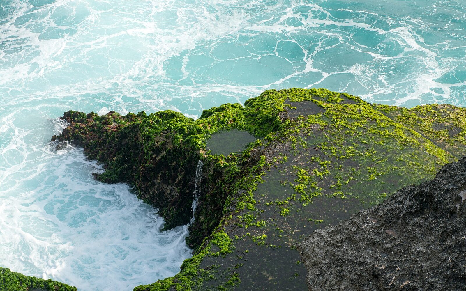 The moss-green 'tear' in the rock where the sea surges up and drains away.