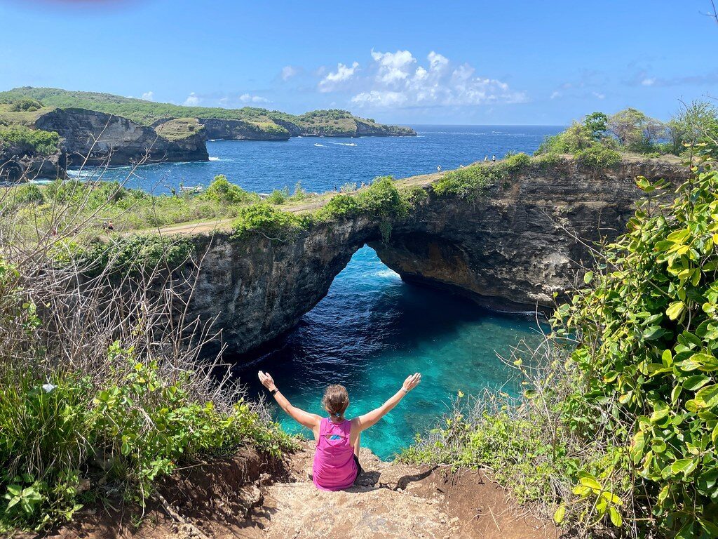 A visitor sitting on the clifftop in front of the Broken Beach arch.