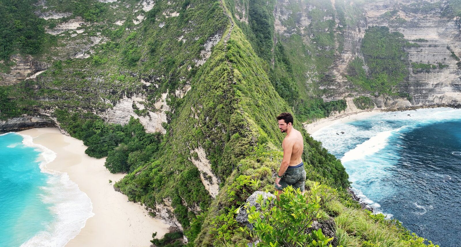A hiker on the steep descent trail, looking down at the beach — the climb people badly underestimate.