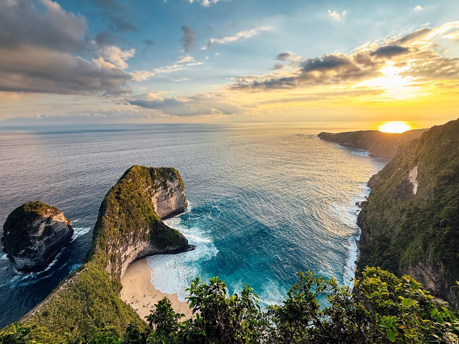 The Kelingking cliff at sunset, the sun dropping into the sea beyond the headland.