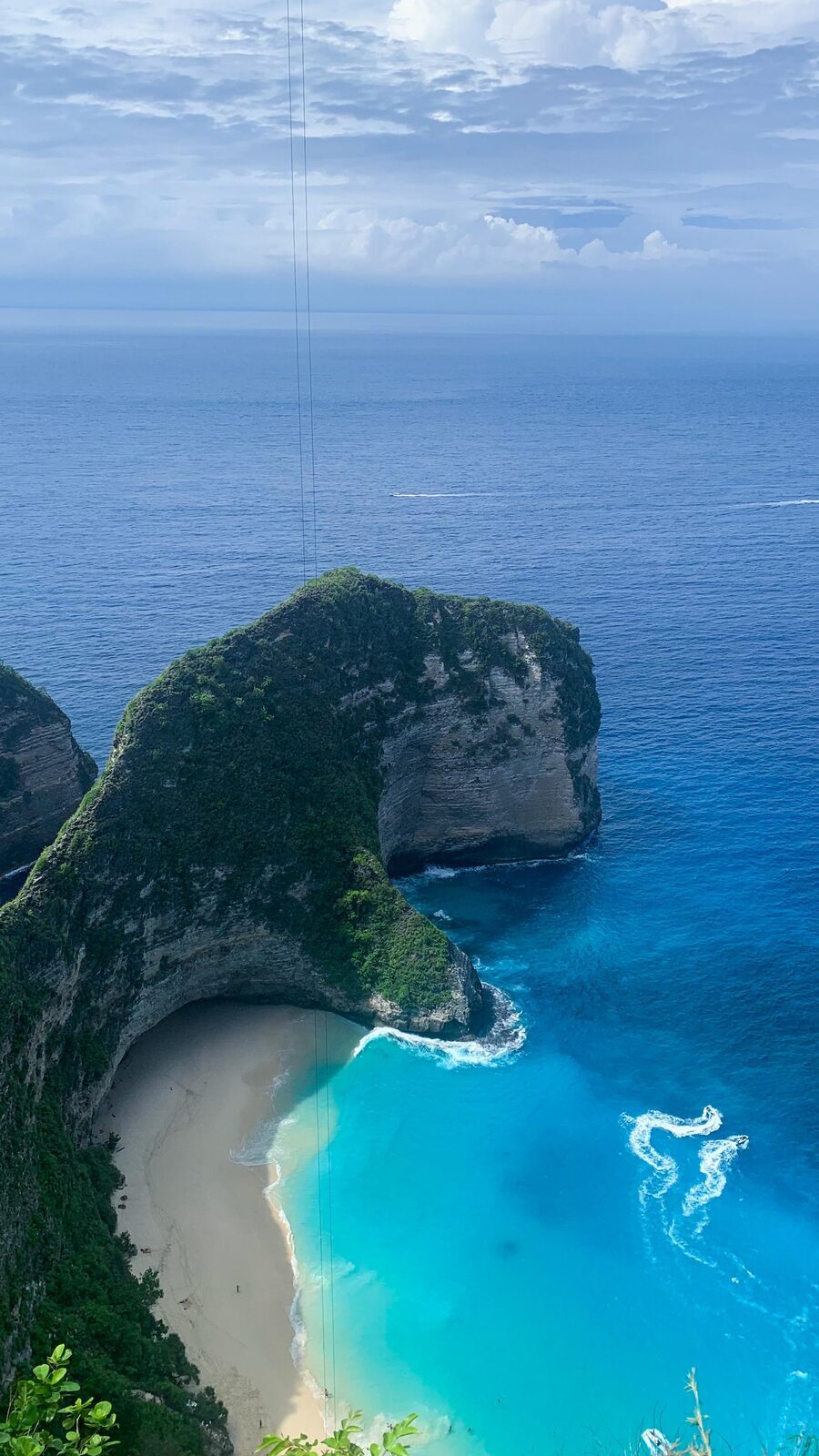 The beach and turquoise cove at the foot of the Kelingking cliff, a small boat offshore.