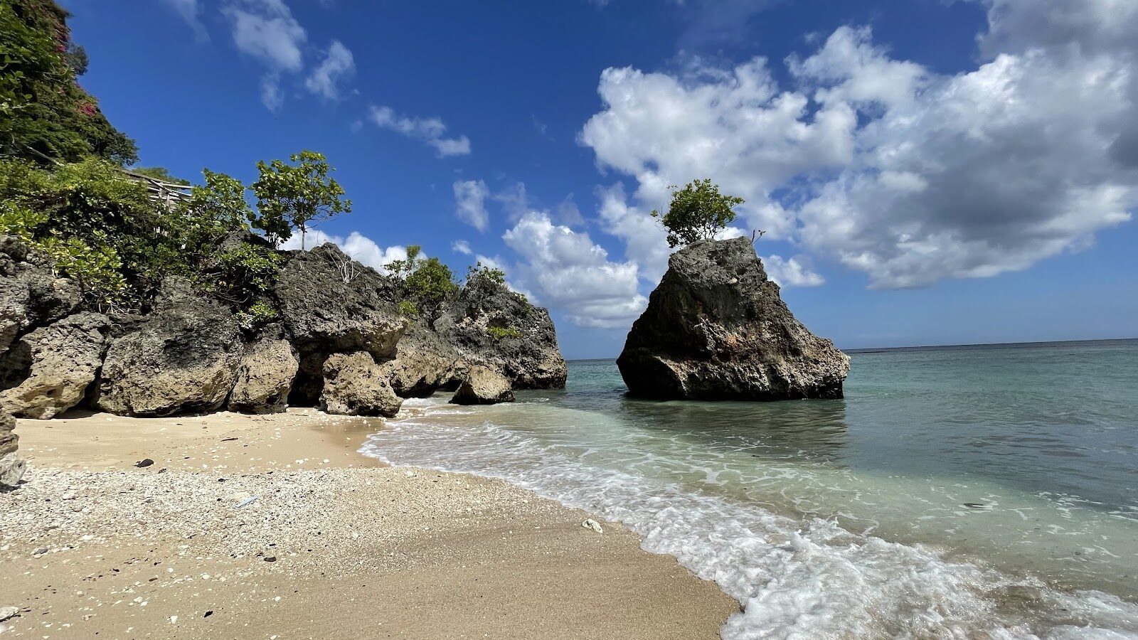 A rock pinnacle on the white sand of a Bukit cove at low tide.