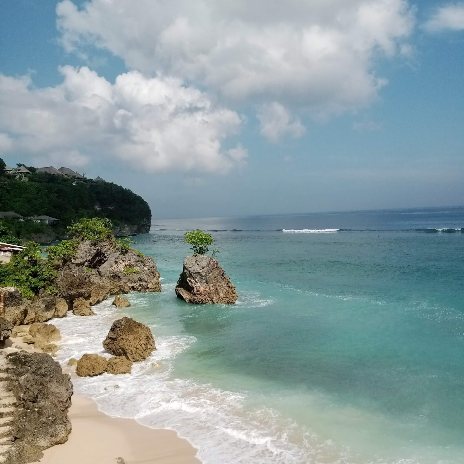 The cove's turquoise shallows and a big rock against the cliff.