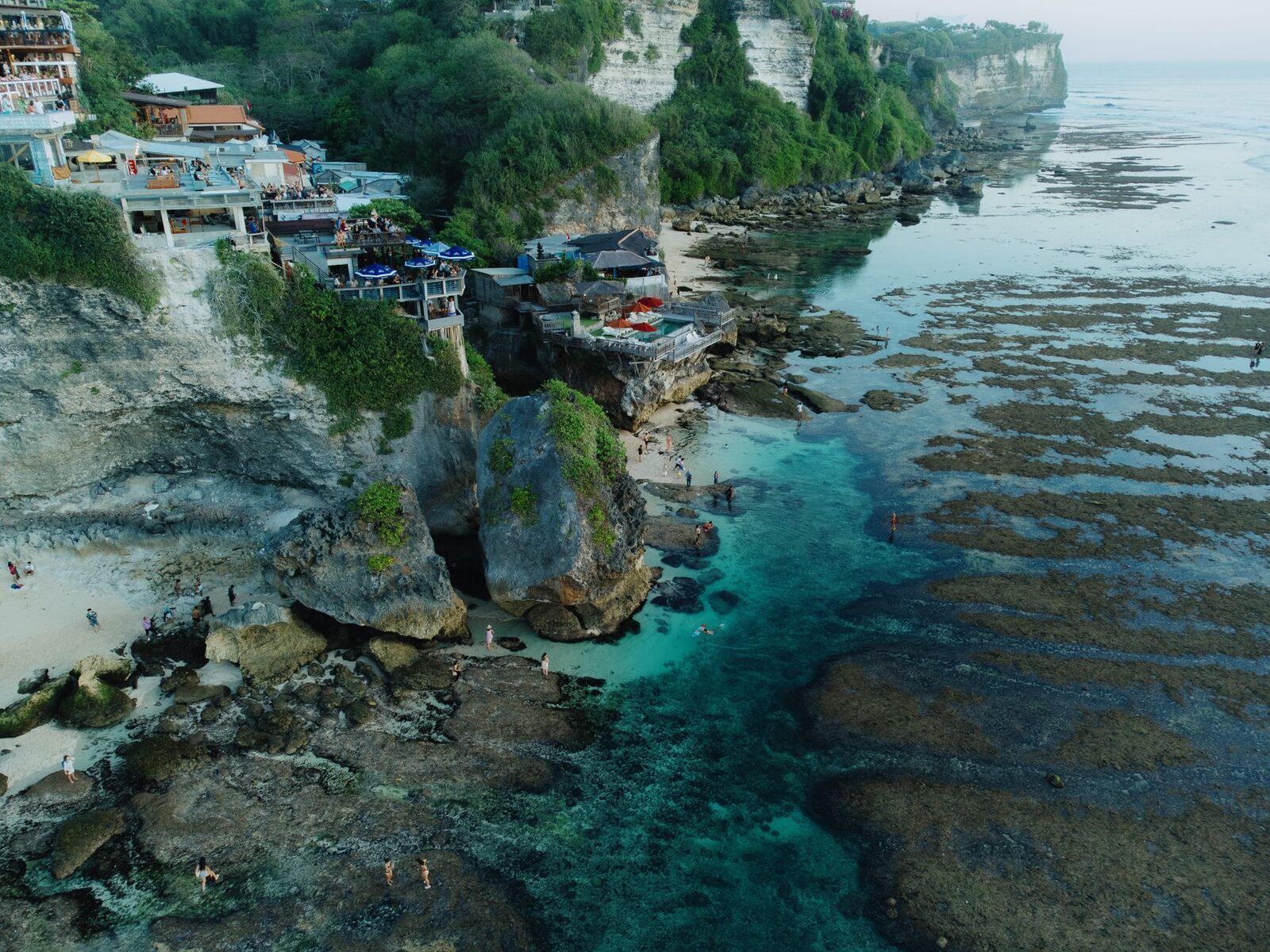 Bingin at low tide from above — clear water and exposed reef below the cliff warungs.