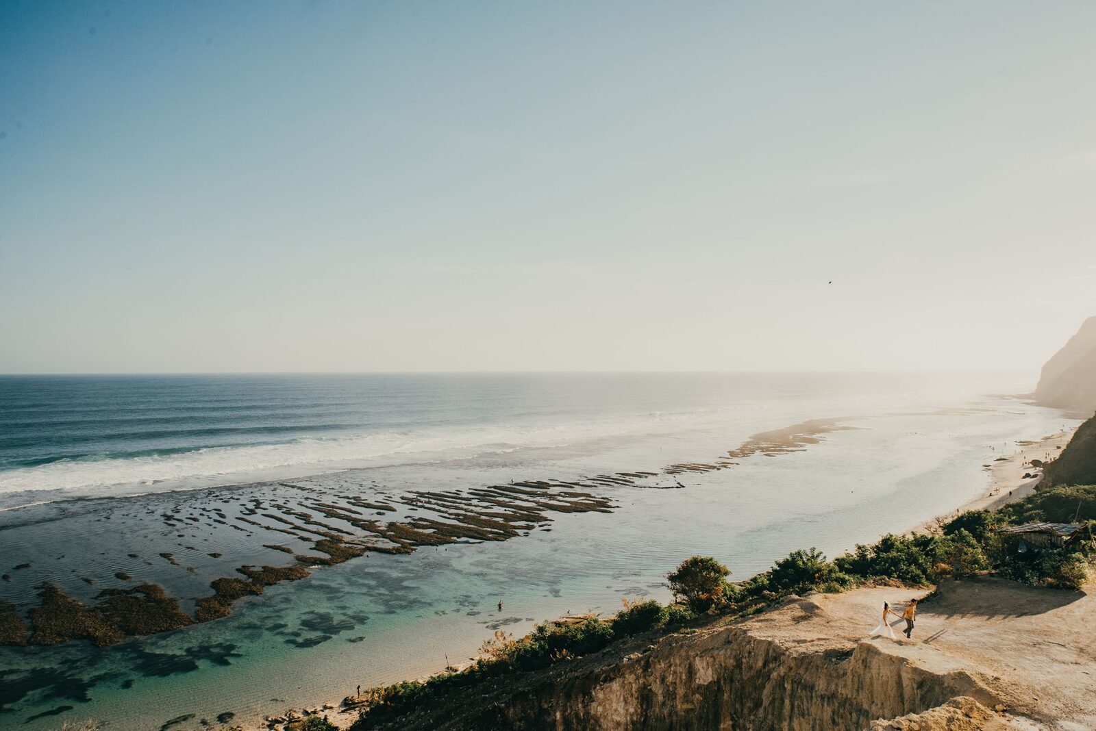The long beach at low tide, reef flats stretching out under the cliff.