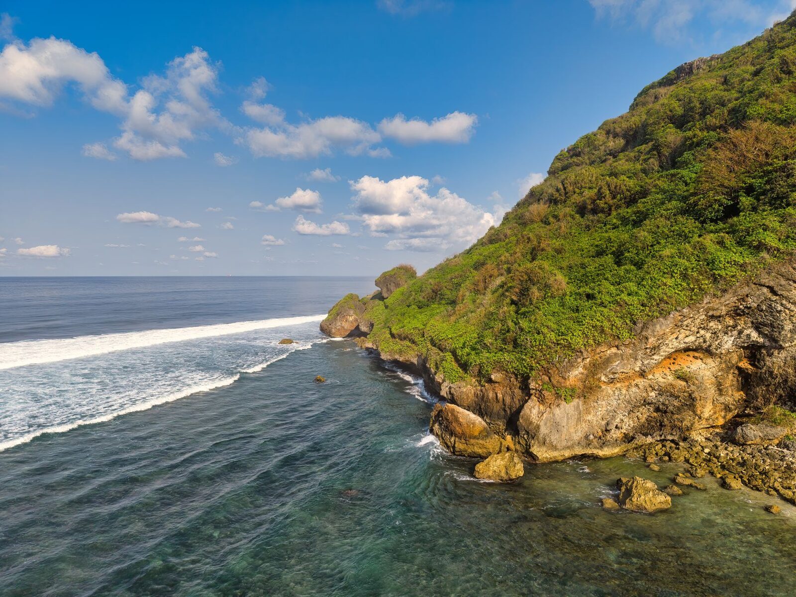 A rugged cliff headland with swell breaking over its reef.