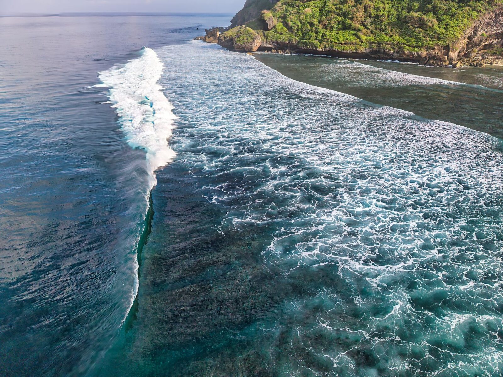 A powerful wave wrapping around a reef point, seen from above.