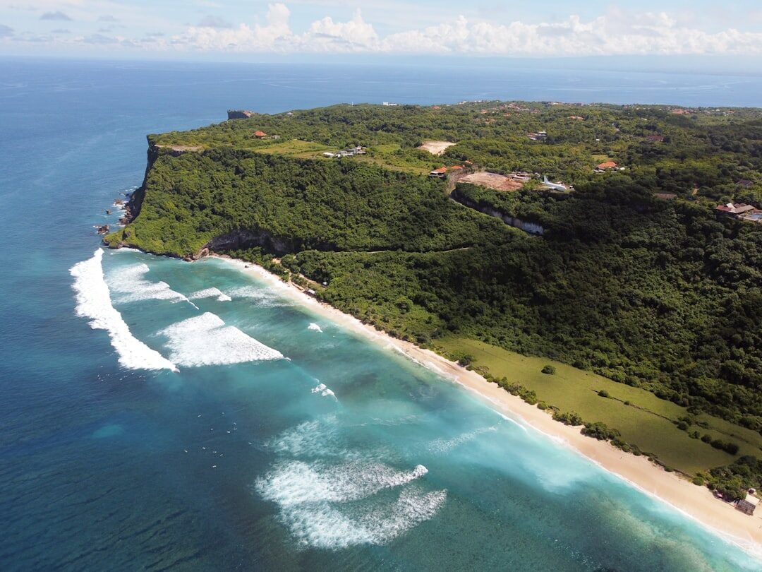The green Bukit headland with white water breaking along its reef.